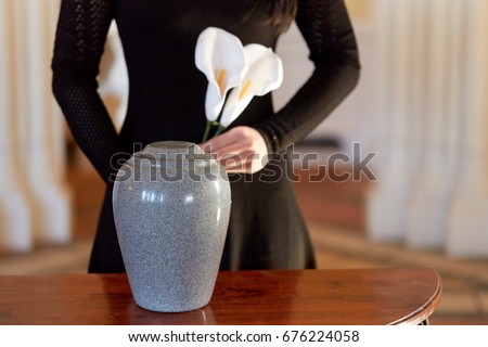 cremation, people and mourning concept - woman with flowers and cinerary urn at funeral in church