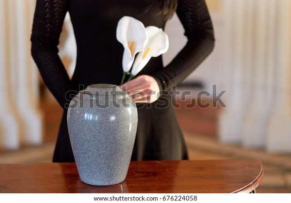 cremation, people and mourning\
concept - woman with flowers and cinerary urn at funeral in\
church