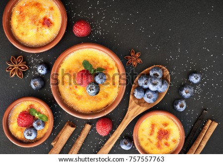 Creme brulee (cream brulee, burnt cream) with raspberry, blueberry and mint in terracota clay baking dishes. Top view, dark stone background.