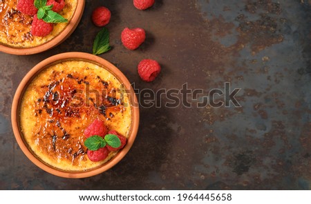 Creme brulee desserts with cream and cane sugar with fresh raspberries and mint leaves in clay bowls on a dark vintage table, mock up with copy space. Delicious desserts in a cafe or restaurant