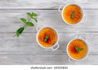 Creme Brulee - French Dessert Of Custard Topped With Caramelized Sugar And Decorated With Mint Leaves In White Ceramic Ramekin On Old Rustic Table, Classic Recipe, View From Above