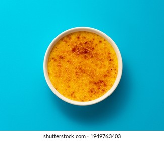 Creme Brulee In Ramekin Isolated On Bright Blue Color Background. Close Up French Dessert. Burned Cream. Spanish Crema Catalana. Top View