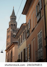 Cremona, Italy - May 5th 2024, Majestic historic bell tower pierces the sky behind charming pastelcolored buildings on a serene european street corner