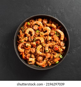 Creole Style Jambalaya With Prawn, Smoked Sausages And Vegetables In Cooking Pan Over Black Stone Background. Top View, Flat Lay