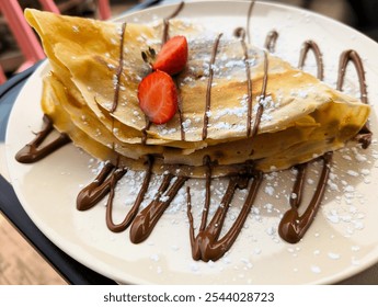 Crepe garnished with chocolate sauce, strawberries and powdered sugar served on a plate, Sweet Desert, close-up - Powered by Shutterstock