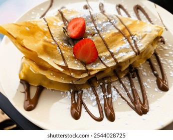 Crepe garnished with chocolate sauce, strawberries and powdered sugar served on a plate, Sweet Desert, close-up - Powered by Shutterstock