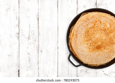 Crepes in a cast iron pan on light wooden background, top view