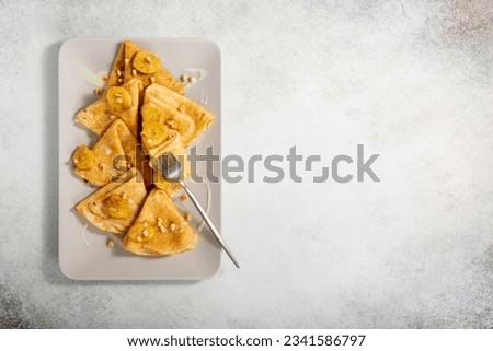 Crepes on rectangular plate on gray background. Thin pancakes served with bananas, pine nuts and sweet sauce. Top view. Copy space.