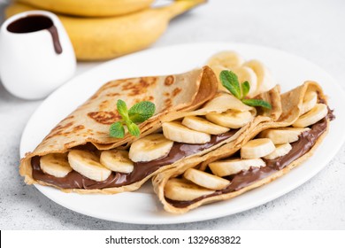 Crepes stuffed with chocolate spread and banana on white plate. Thin pancakes, blini. Sweet dessert.