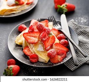 Crepes stuffed with cream cheese and fresh fruit; strawberries and raspberries sprinkled with powdered sugar on a black plate,  close up - Powered by Shutterstock