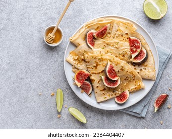 Crepes (thin pancakes, blini) with sliced fig, lime zest and honey on plate, light grey table. Top view. Copy space. Festive breakfast, lunch, dessert or snack. Maslenitsa, shrovetide, pancakes week.