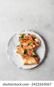 Crepes o tortas finas con salmón ahumado, queso blando y espinacas sobre la mesa aisladas en fondo gris texturado. Día del panqueque, Maslenitsa. Vertical