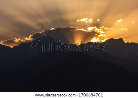 Crepuscular light rays of the setting sun scatter behind the Himalayan mountains and the clouds in the village of Nako in Kinnaur in Himachal Pradesh, India.