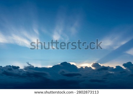 Crepuscular rays are shining from behind a cluster of rain clouds.