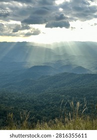 Crepuscular rays shining through dramatic clouds over a vast green mountain forest and valley