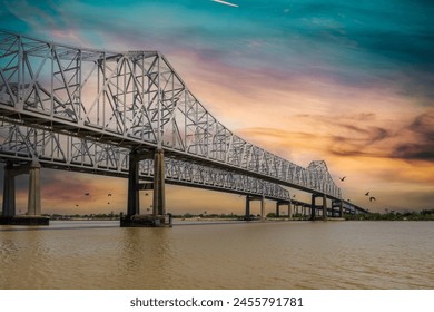 The Crescent City Connection bridge over the Mississippi River with lush green trees, plant and grass and powerful clouds at sunset in New Orleans Louisiana USA  - Powered by Shutterstock