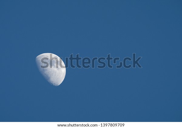 A
crescent moon being visible in daytime.  Rising in the East,
hanging high, a pale impression against a background of beautiful
clear blue sky.  Wallpaper and texture with copy
space.