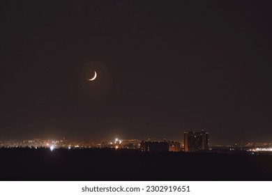 A crescent moon in the night sky is setting over the horizon. New moon on the background of the night city - Powered by Shutterstock