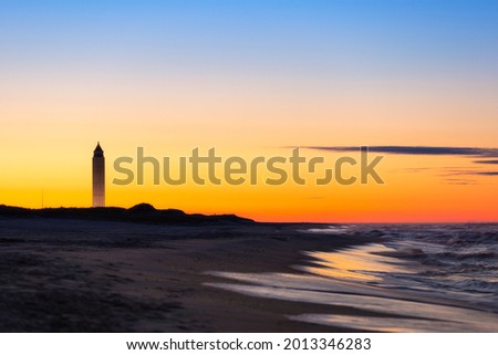 Crescent moon rising just before sunrise next to a tall tower on the beach. Jones Beach State Park, New York