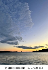 Crescent moon rising over dramatic clouds at twilight with calm sea reflection