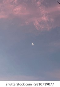 Crescent moon visible through soft clouds in a twilight sky, creating a peaceful and minimalist celestial landscape.