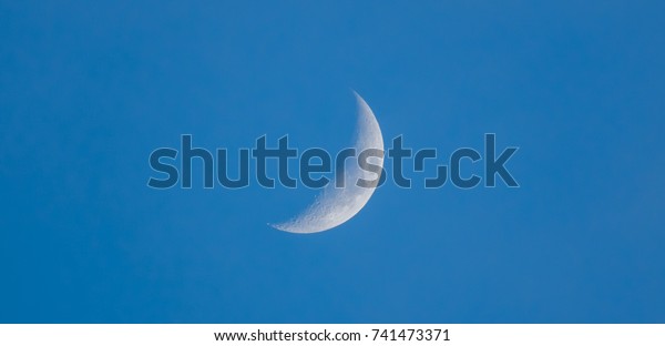 Crescent shape moon or gibbous on day and\
beautiful blue sky. Lunar phases change cyclically as Moon orbits\
the Earth. It changing positions Sun relative and Earth. Moon is\
right side waxing\
crescent.
