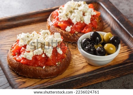 Cretan dakos is for a traditional salad from the island of Crete consists of barley rusk topped with juicy tomatoes, cheese and olive oil closeup on the wooden board on the table. Horizontal