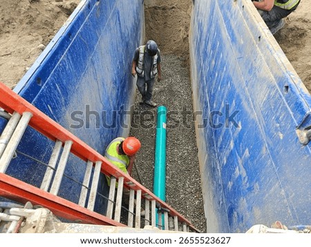 Crew inspects initial SDR35 segment for alignment and surface defects while awaiting next pipe delivery inside shored trench for sanitary main install.