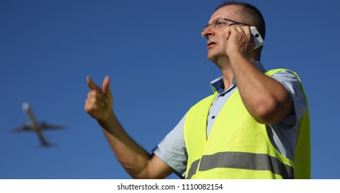 Crew Man Working And Talking On Mobile Phone With Air Traffic Control Tower In Airport While Airplane Passing Overhead