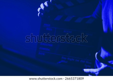 A crew member prepares to mark the beginning of a new take with a clapperboard in a dimly lit film studio while the atmosphere is charged with anticipation.