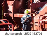 A crew member working on deck of a merchant ship, using a pneumatic tool to remove rust. Focused on preparing the surface for painting and maintenance, ensuring the ship