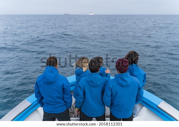 Crew members in blue uniforms standing on a\
boat dividing the sea and other\
boats.