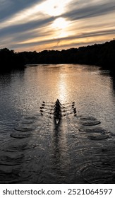 a crew team of rowers making ripples with their oars on a calm lake at sunset
