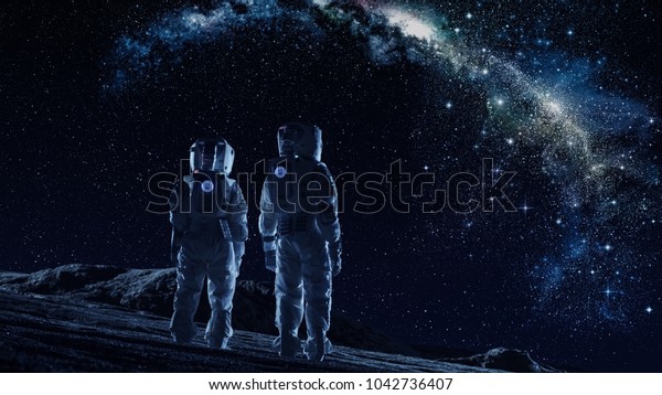 Crew of Two Astronauts in Space Suits\
Standing on the Moon Looking at the The Milky Way Galaxy. High Tech\
Concept of Moon Colonization and Space\
Travel.