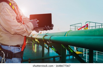 Crew Worker On Oil Tanker Storage Ship And Hand Holding Ipad Wearing Safety Full Harness With Green Pipe Line Connect Existing On Deck.