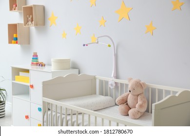 Crib with toy bear in stylish baby room interior