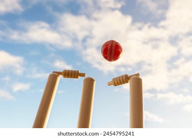 Cricket ball hitting wicket stumps knocking bails out against blue sky background - Powered by Shutterstock