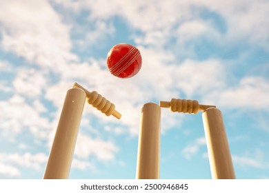 Cricket ball hitting wicket stumps knocking bails out against blue sky background