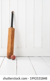 Cricket bat and ball against white wall and floor.
