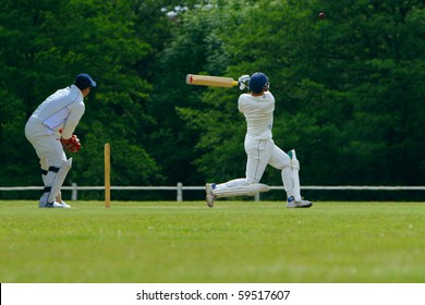 A cricket batsman playing a pull shot towards the boundary in a cricket match while the catcher looks on.