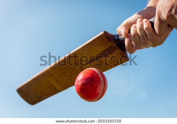Cricket player batsman hitting a ball with a bat\
shot from below against a blue\
sky