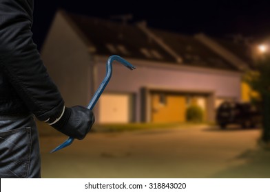 Crime concept. Burglar or robber with crowbar stands in front of the house at night.