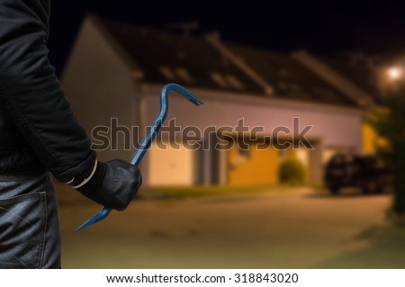 Crime concept. Burglar or robber with crowbar stands in front of the house at night.