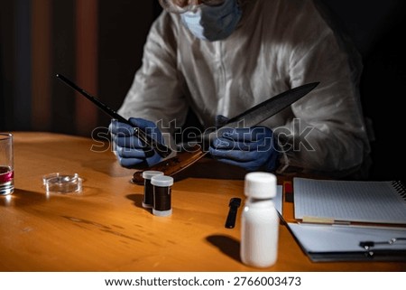 Crime scene evidence processing on wooden desk: gloved hands use a brush to reveal latent prints on a drinking glass beside a knife with blood stains and sample vials.