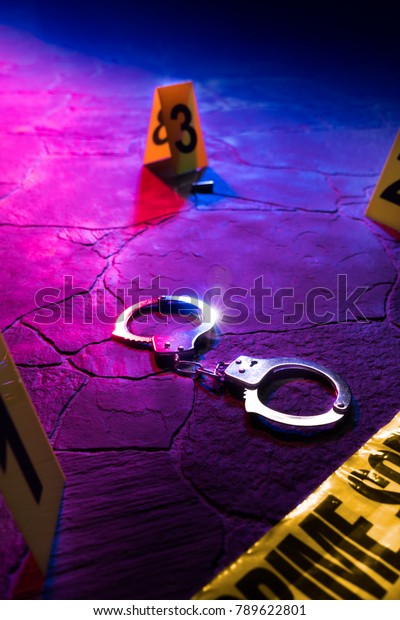 Crime scene at night with closed handcuffs on the\
street pavement, police car lights and evidence markers / high\
contrast image