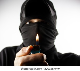 The Criminal In A Black Mask With A Burning Lighter. The Concept Of Arson, Crime, Mafia.