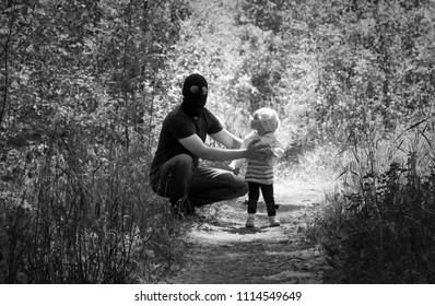 A Criminal In A Black Mask Is Holding A Child In The Forest, A Hostage, Stealing Children