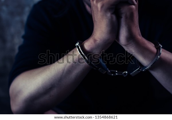 Criminal concept. Bad guy was cuffed and under\
arrest by policeman and detain prisoner in the jail. Detainees\
waiting someone for bailing out him from prison. Young prisoner\
sitting in dark room