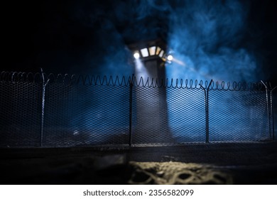 Criminal justice imprisonment concept. Old prison watchtower protected by wire of prison fence at night. Creative art decoration. Selective focus