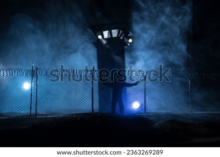Criminal justice imprisonment concept or prison break concept. Silhoette of prisoner standing near of prison fence with watchtower at night. Creative art decoration. Selective focus